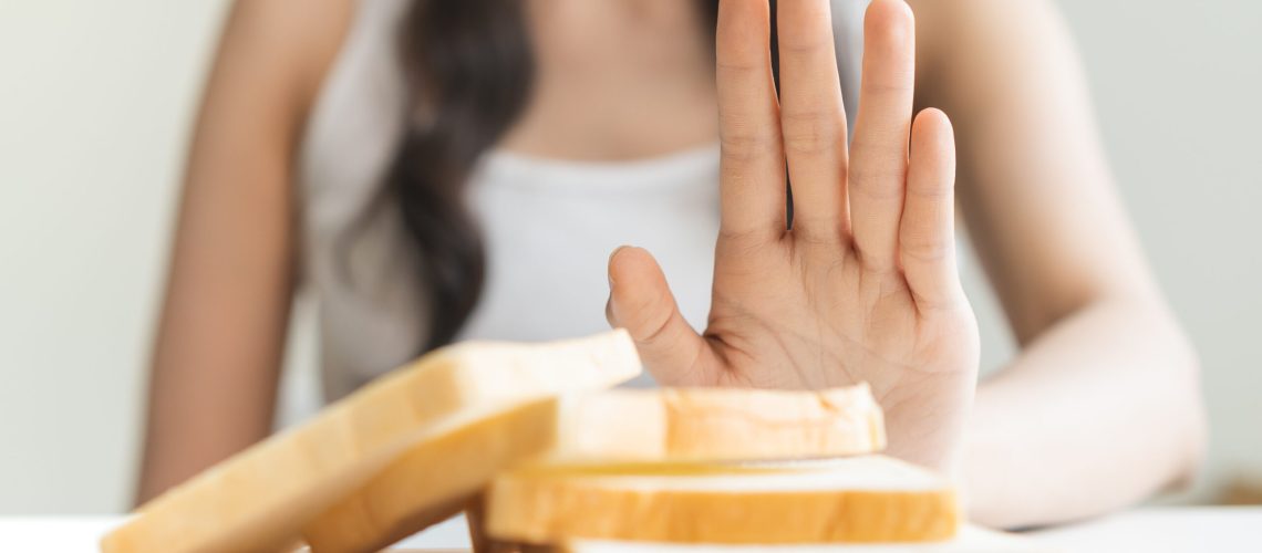 Gluten allergy, asian young woman hand push out, refusing to eat white bread slice on chopping board in food meal at home, girl having a stomach ache. Gluten intolerant and Gluten free diet concept.